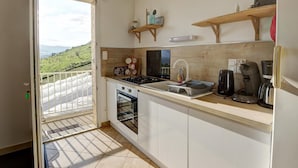 A kitchen with a gas stove, oven, and coffee maker. There is a window with a view of a green landscape. - Rural lodge with garden and children's play area (Saint-Romain-en-Jarez)