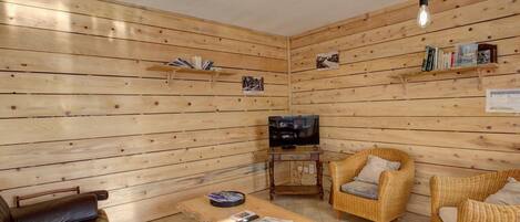 A cozy room with wooden walls, a television, wicker furniture, and shelves with books and pictures.