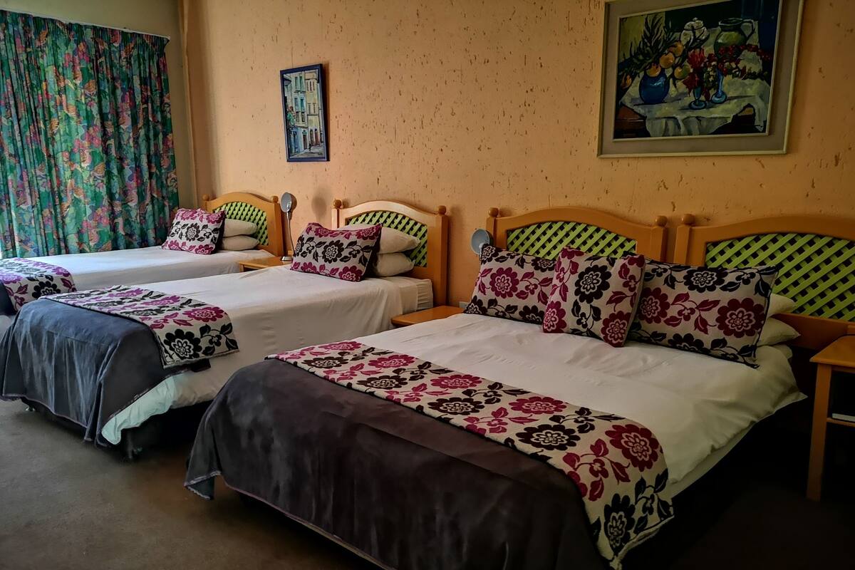 Ein Hotelzimmer mit zwei Einzelbetten, beide mit blumigem Bettbezug und Kopfteilen. An der Wand hängt ein Gemälde, und ein Vorhang mit floralem Muster ist zu sehen.