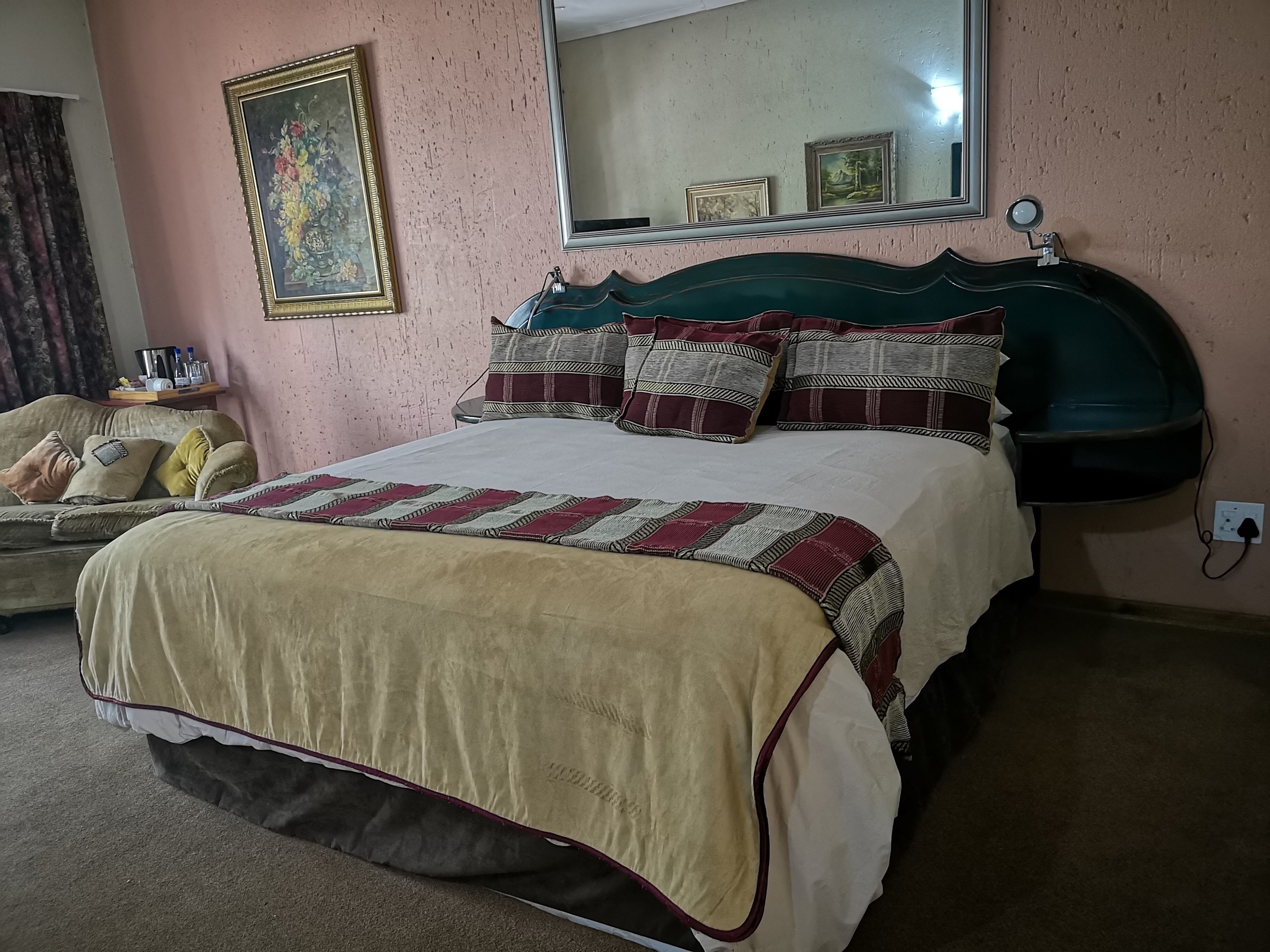 A bedroom with a bed, a sofa, a mirror, and a wall with framed pictures.