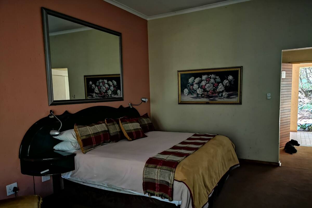 Ein Schlafzimmer mit einem Bett, einem großen Spiegel und zwei gerahmten floralen Bildern an der Wand.