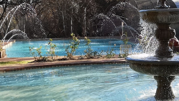 Una piscina cristalina con una fuente en primer plano y árboles al fondo.