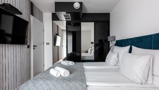 Una habitación de hotel con una cama grande, un televisor montado en la pared y un espejo que refleja el cuarto.