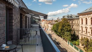 Un balcón con una mesa y sillas, con vista a una calle con edificios históricos y un cielo despejado.