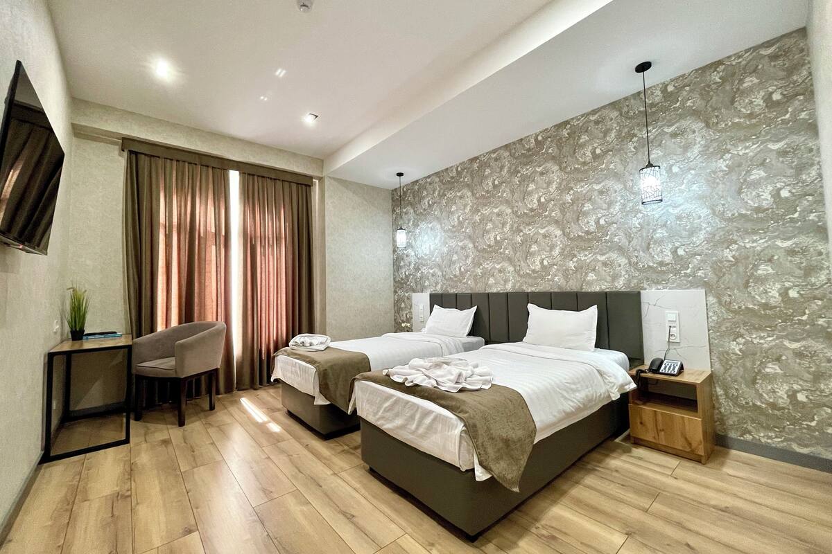 A modern hotel room with two beds, a desk, a chair, and a TV.