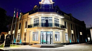 A hotel with a prominent entrance, multiple flags, and a well-lit sign above the entrance. - Alpha Plaza (Tashkent)