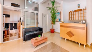 Un hall d’hôtel avec un comptoir d’accueil, un canapé en cuir noir, une table basse en bois et une plante en pot.