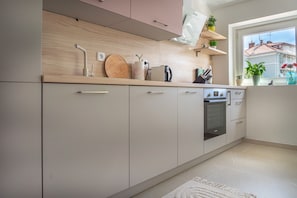Une cuisine moderne avec des meubles de couleur bois clair, un four encastré et une fenêtre donnant sur des immeubles.