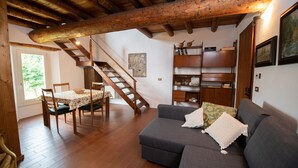 Una sala de estar acogedora con una escalera de madera, un sofá gris y un comedor con mesa y sillas.