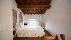 Un dormitorio con techo de madera, una cama con colcha blanca, una silla de madera y una pared de piedra.