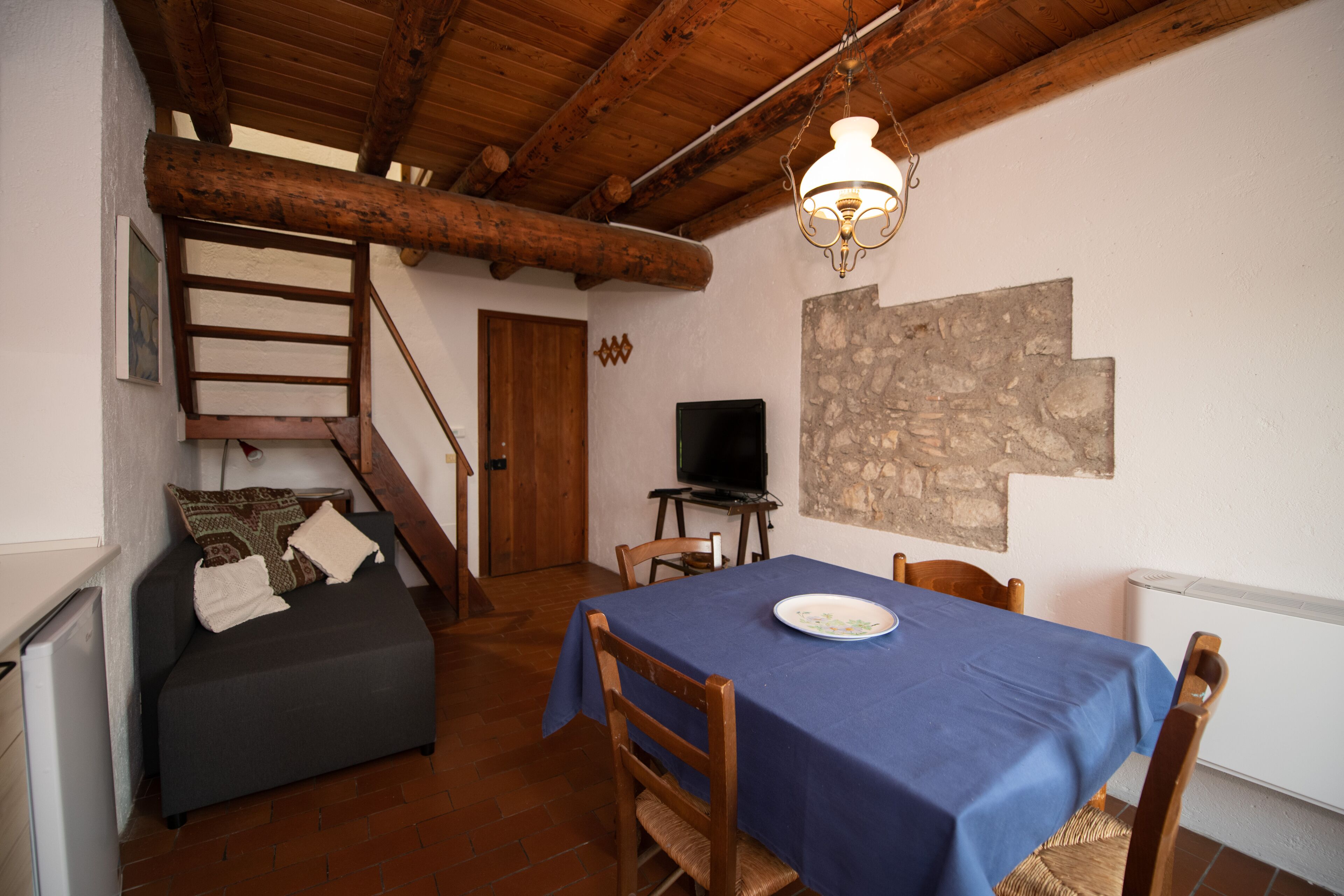 Ein gemütliches Zimmer mit einem blauen Tisch, Holzstühlen, einer kleinen Couch, einem Fernseher und einer Treppe.