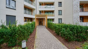 A multi-story residential building with a central courtyard, a covered entrance, and a pathway flanked by greenery.