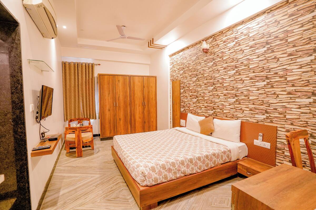 A hotel room with a bed, wooden furniture, a stone wall, and a television.
