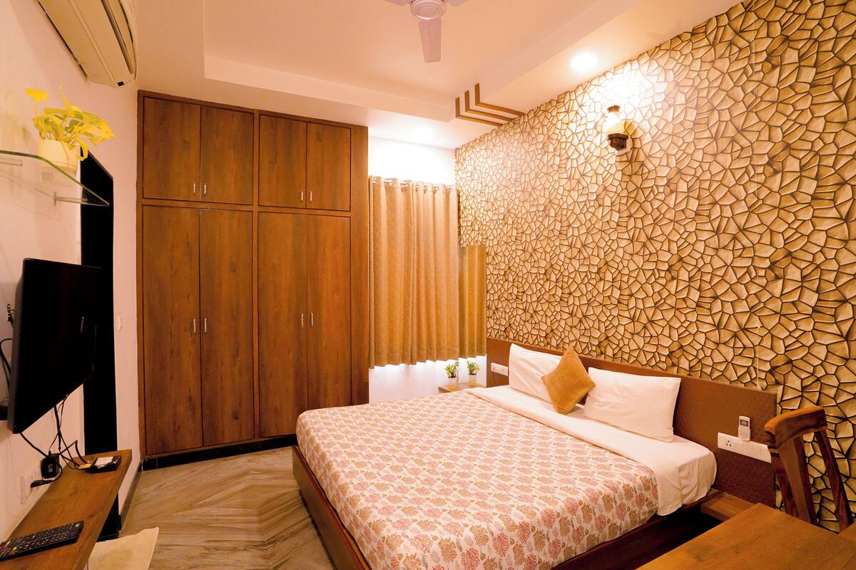 A hotel room with a bed, wooden wardrobe, and a decorative wall.