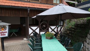 An outdoor dining area with a table covered by a green tablecloth, surrounded by green plastic chairs. There is a sign with the text "Rothaus Bräu" and a large umbrella providing shade. - Wonderful private villa for 18 people with WIFI, TV, terrace and pets allowed (Nonnenbach)
