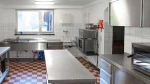 A kitchen with a checkered floor, stainless steel appliances, a large table, and a window with blinds. - Wonderful private villa for 18 people with WIFI, TV, terrace and pets allowed (Nonnenbach)