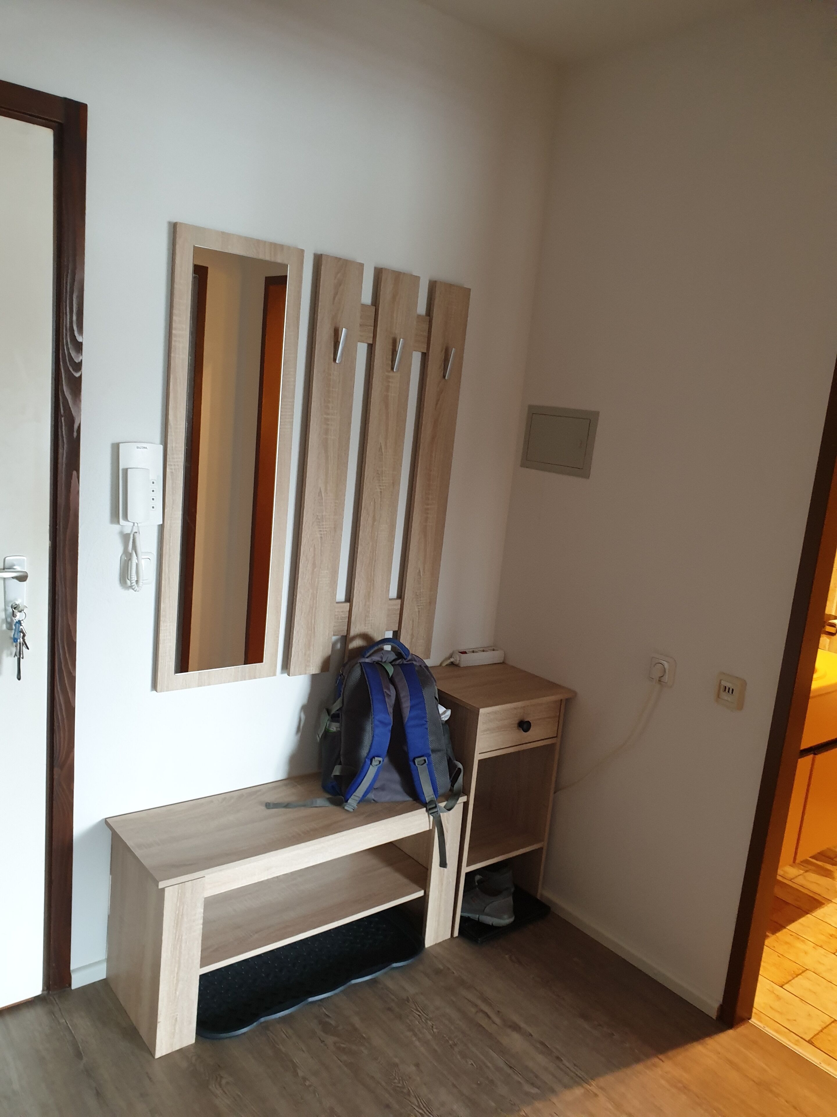 A room with a wooden bench, a wall-mounted mirror, a blue backpack, and a small wooden table.