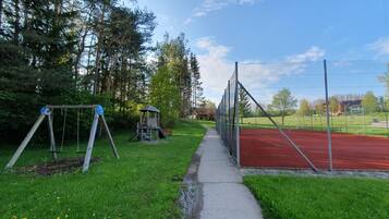 A playground with swings and a small playhouse, a red running track, and a pathway.