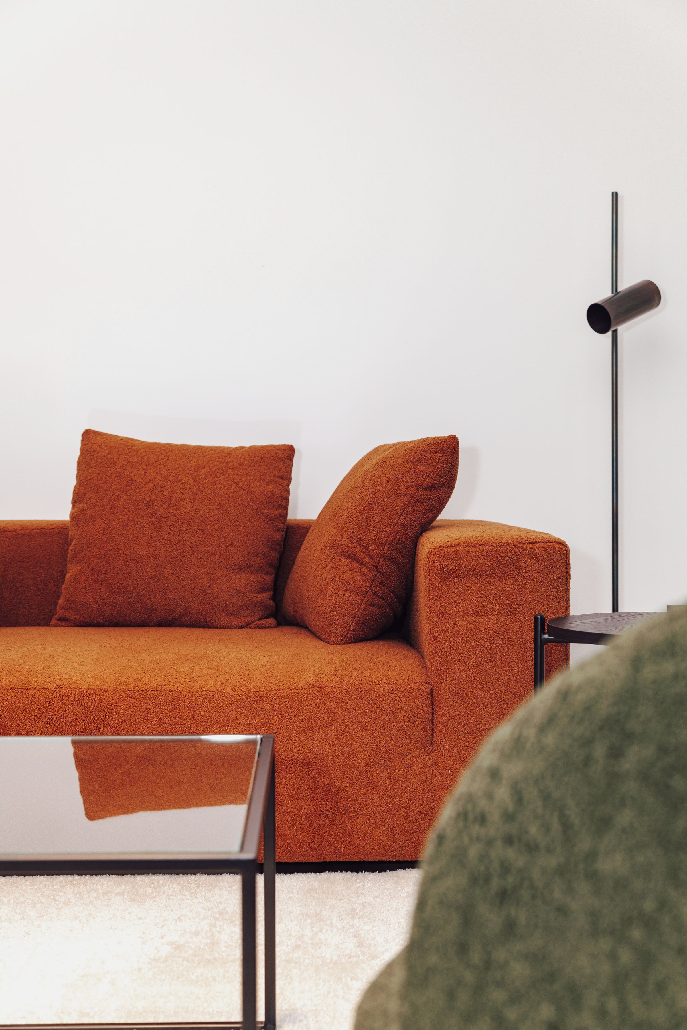 Un salon moderne avec un canapé, des coussins, une lampe sur pied et une table basse en verre.