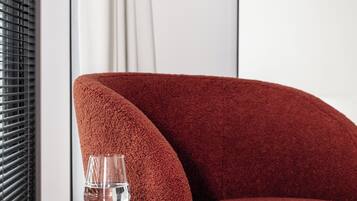 Een rode fauteuil met een glas water en een notitieboekje op een klein tafeltje ernaast.