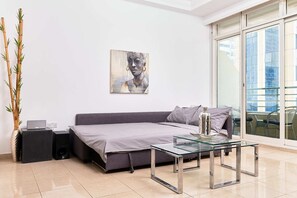 A modern living room with a grey sofa, a glass coffee table, and a large window with a city view.