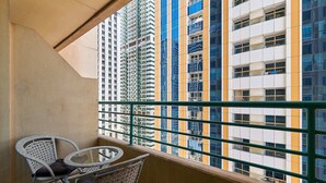 A balcony with wicker chairs and a small table, overlooking a high-rise building with multiple balconies. - Cozy 1BR apartment Marina Crown (Dubai)