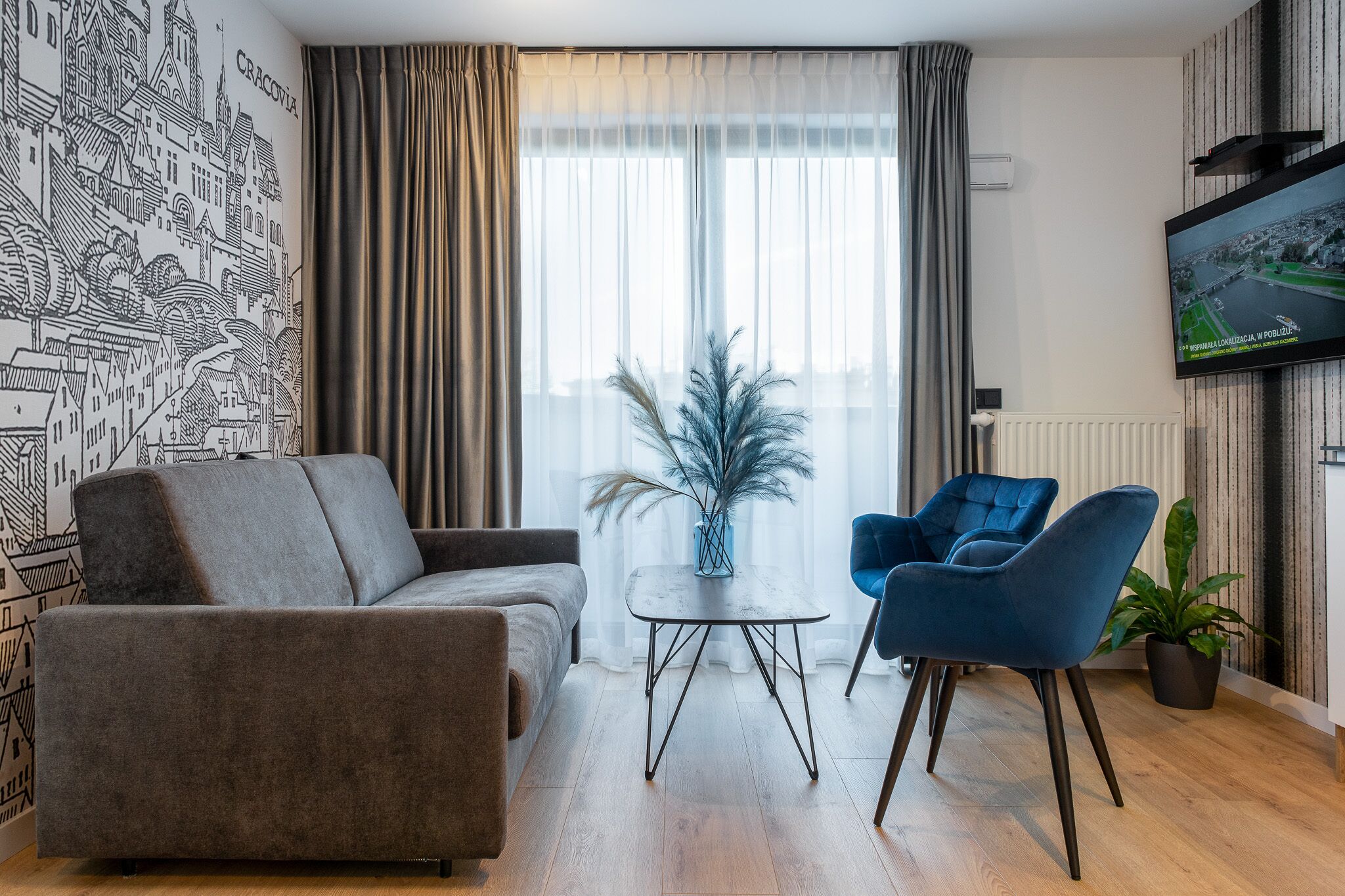A modern living room with a sofa, a coffee table, and two blue chairs. A large window with sheer curtains allows natural light to fill the room.