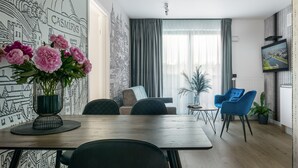 Moderni olohuone, jossa on puinen ruokapöytä, siniset tuolit, sohva ja suuri ikkuna, jossa on verhot.