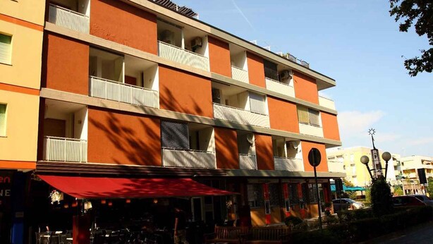 A multi-story hotel with balconies, outdoor seating, and a red awning.