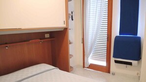 A bedroom with a bed, a wooden wardrobe, a window with blinds, and a blue chair.
