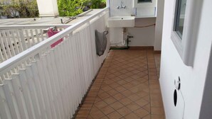 A narrow corridor with a tiled floor, a white railing, and a window on the right.