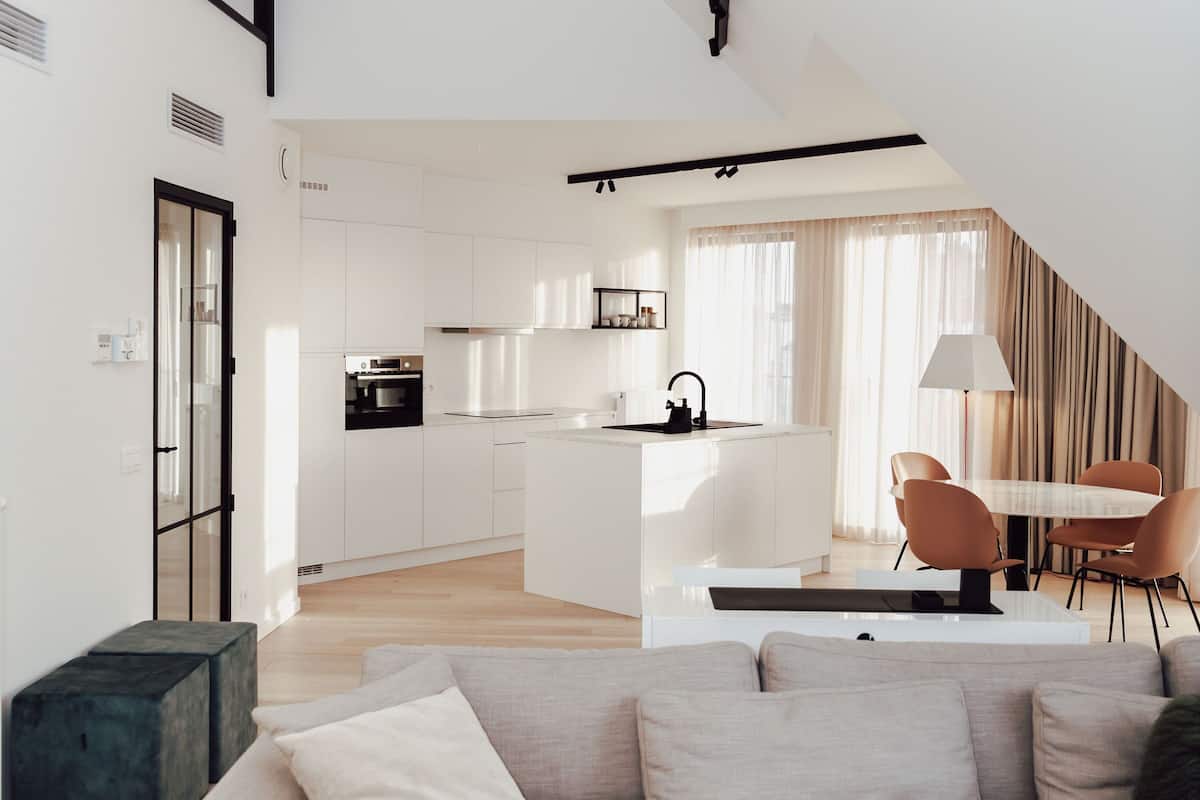 A modern living space with a sofa, a dining table with chairs, a kitchen area, and a staircase.