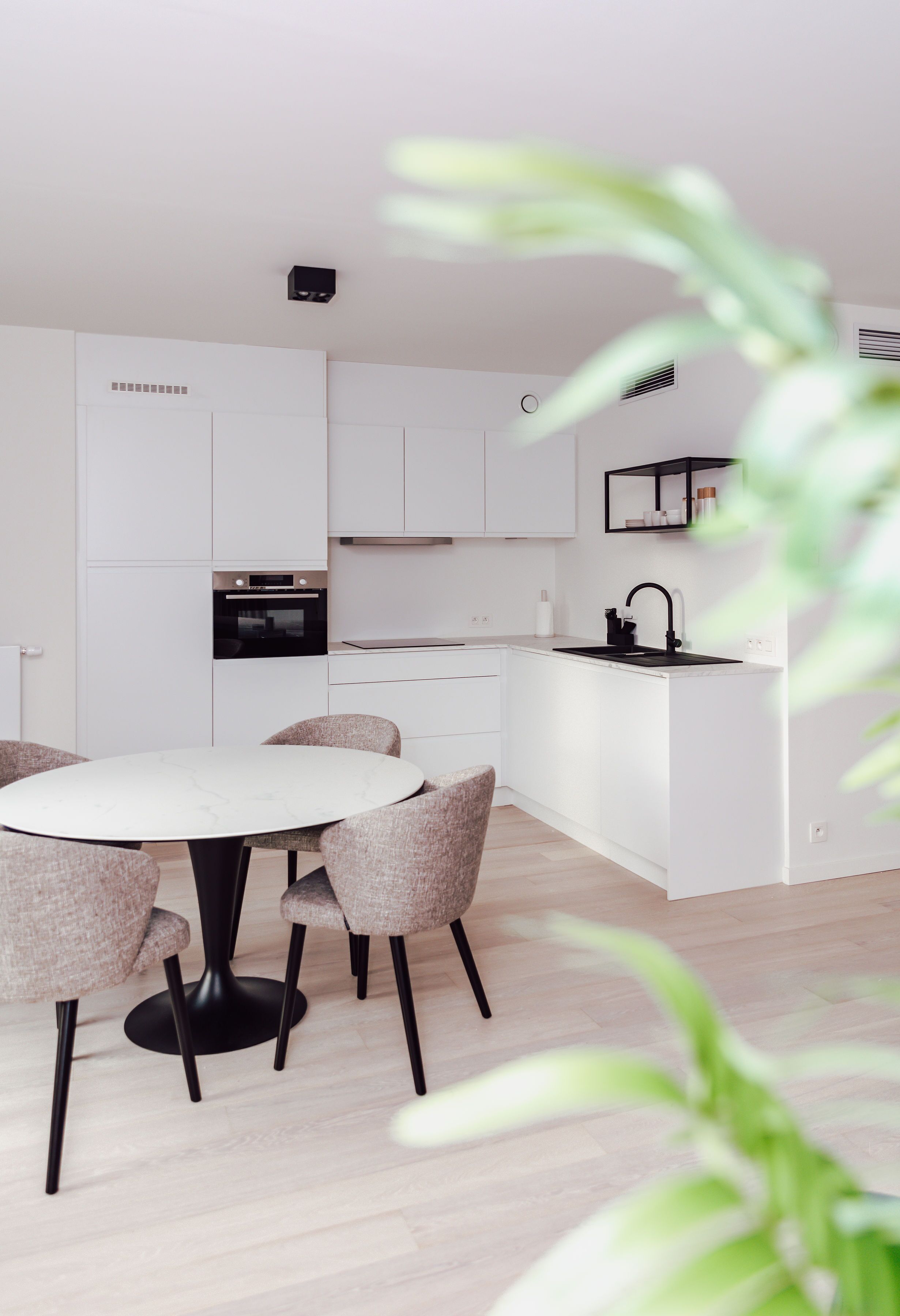 Une cuisine moderne avec des meubles blancs, un four noir et une table de salle à manger ronde, accompagnée de quatre chaises.