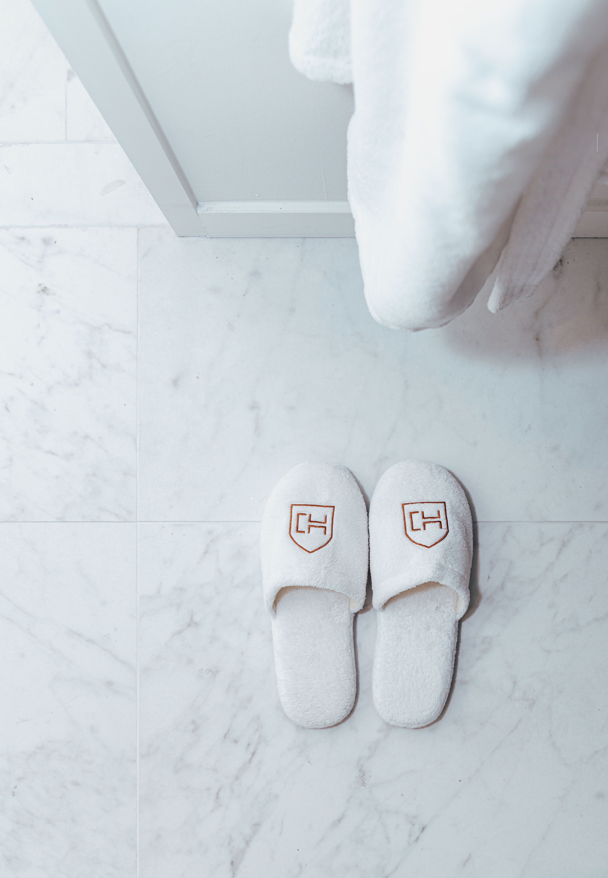 A pair of white slippers with a logo on a white tiled floor.
