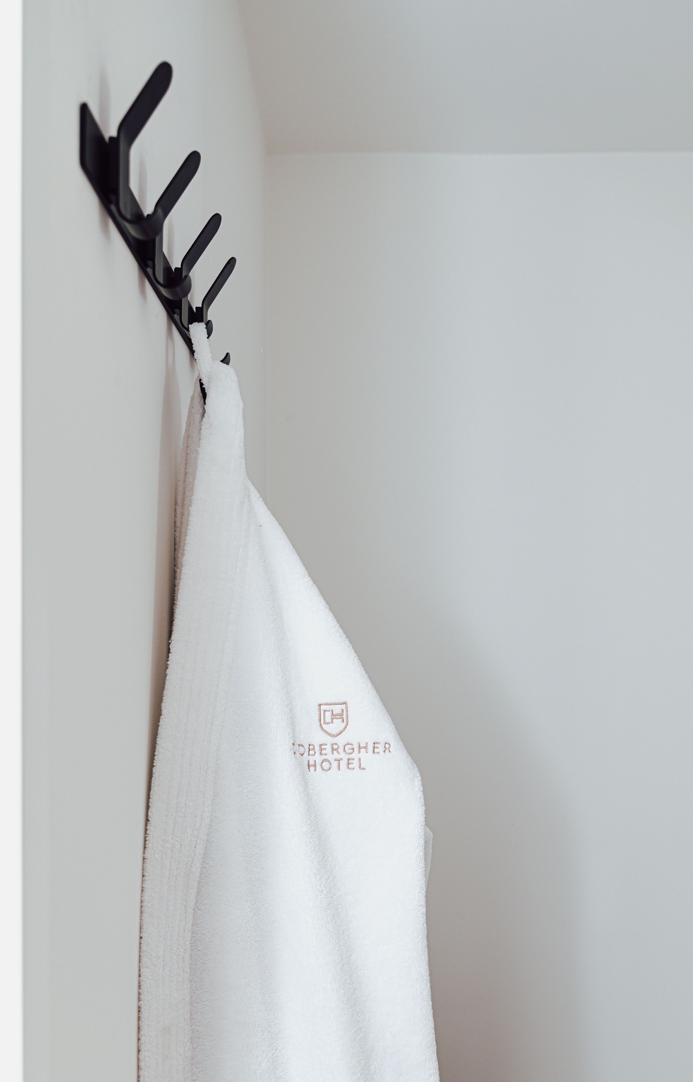 A white towel hanging on a black wall-mounted rack with a hotel logo.