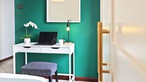 Une pièce avec un bureau blanc, un ordinateur portable, une orchidée en pot, une tasse et un luminaire moderne.