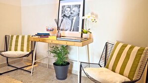 Une pièce avec deux chaises à rayures, un petit bureau sur lequel est posée une photo encadrée, une plante en pot et un vase rempli de fleurs.