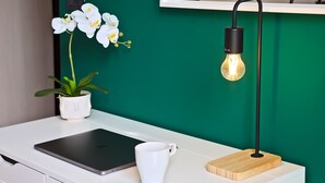 Un bureau blanc avec un ordinateur portable, une tasse blanche, une orchidée en pot et une lampe de bureau moderne avec une ampoule.