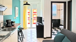 Une cuisine moderne équipée d’un évier, d’une cuisinière et de tabourets de bar, un coin repas avec une table et des chaises, et un salon avec un canapé et des coussins.