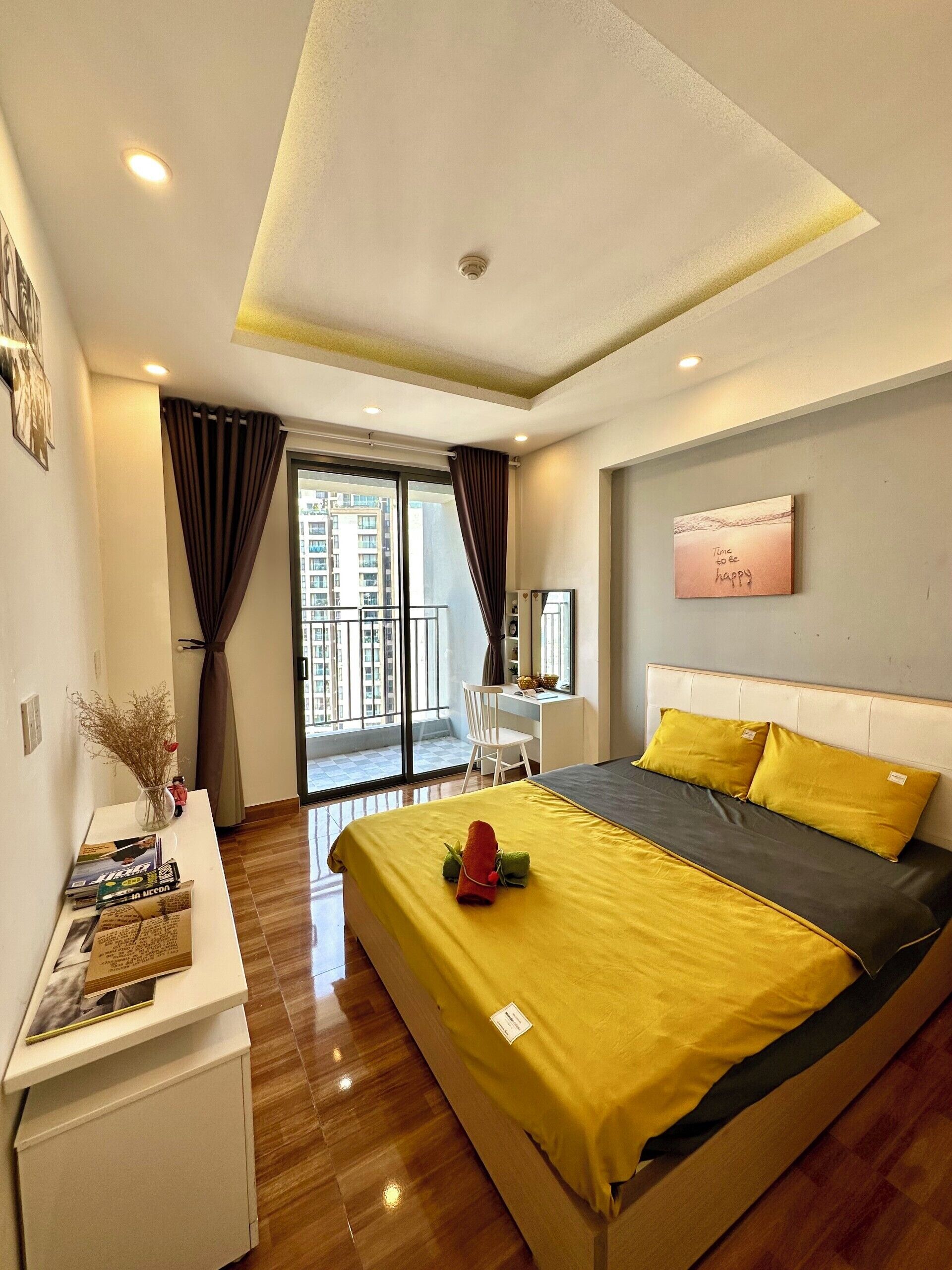 A hotel room with a bed, a desk, a chair, a small table with a vase, and a window with curtains.