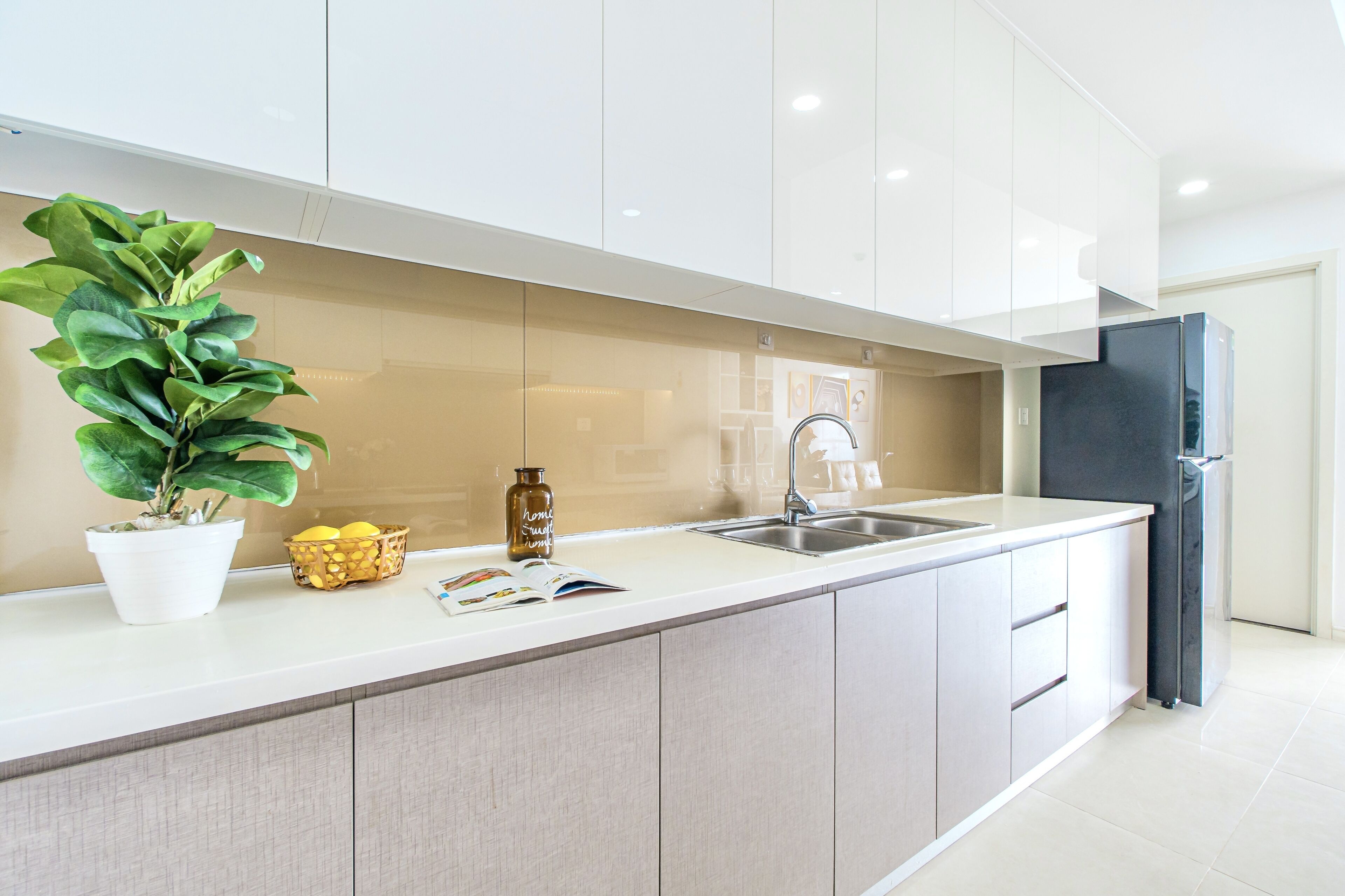 Eine moderne Küche mit weißer Arbeitsplatte, einem Spülbecken, einem schwarzen Kühlschrank und einem Blumentopf.