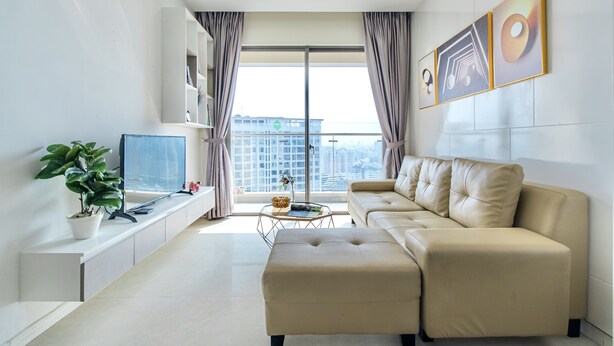 Una sala de estar moderna con un sofá, un televisor, una planta y vistas de la ciudad a través de grandes ventanales.
