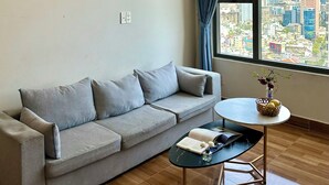 Una sala de estar moderna con un sofá gris, una mesita redonda con un jarrón y vistas a la ciudad a través de amplias ventanas.
