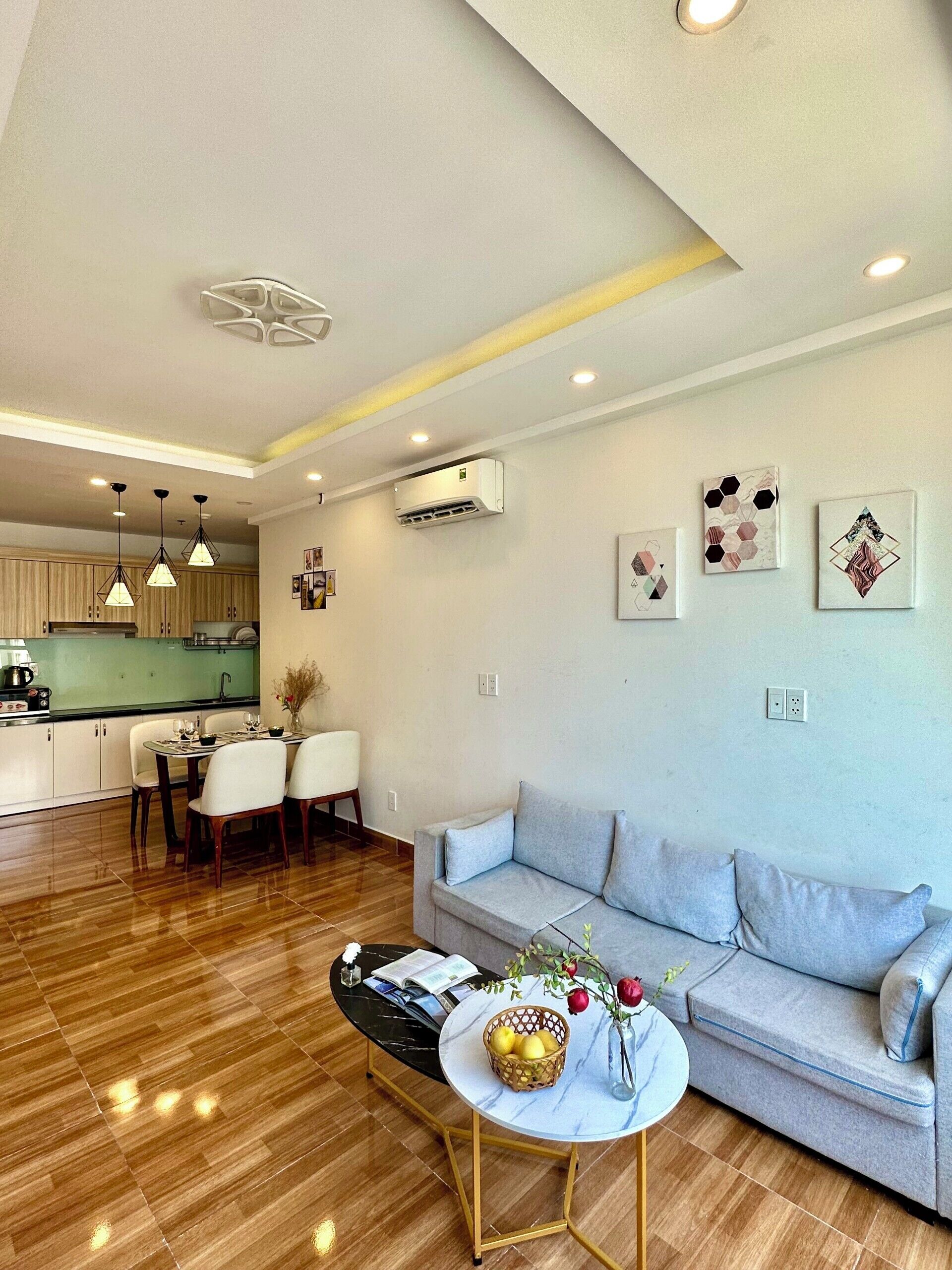 A modern living room with a grey sofa, a coffee table with a basket and vase, wooden flooring, and a kitchen in the background.