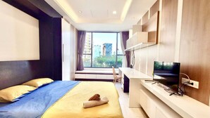 Habitación de hotel moderna con cama, escritorio con televisor y un ventanal que ofrece vistas a la ciudad.