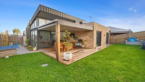 A modern house with a covered patio, a brick exterior, and a well-maintained lawn. - Amongst The Tea Trees (Inverloch)