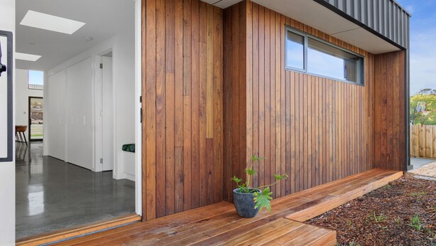 A modern house with a wooden exterior, a large window, and a potted plant on the porch. - Amongst The Tea Trees (Inverloch)