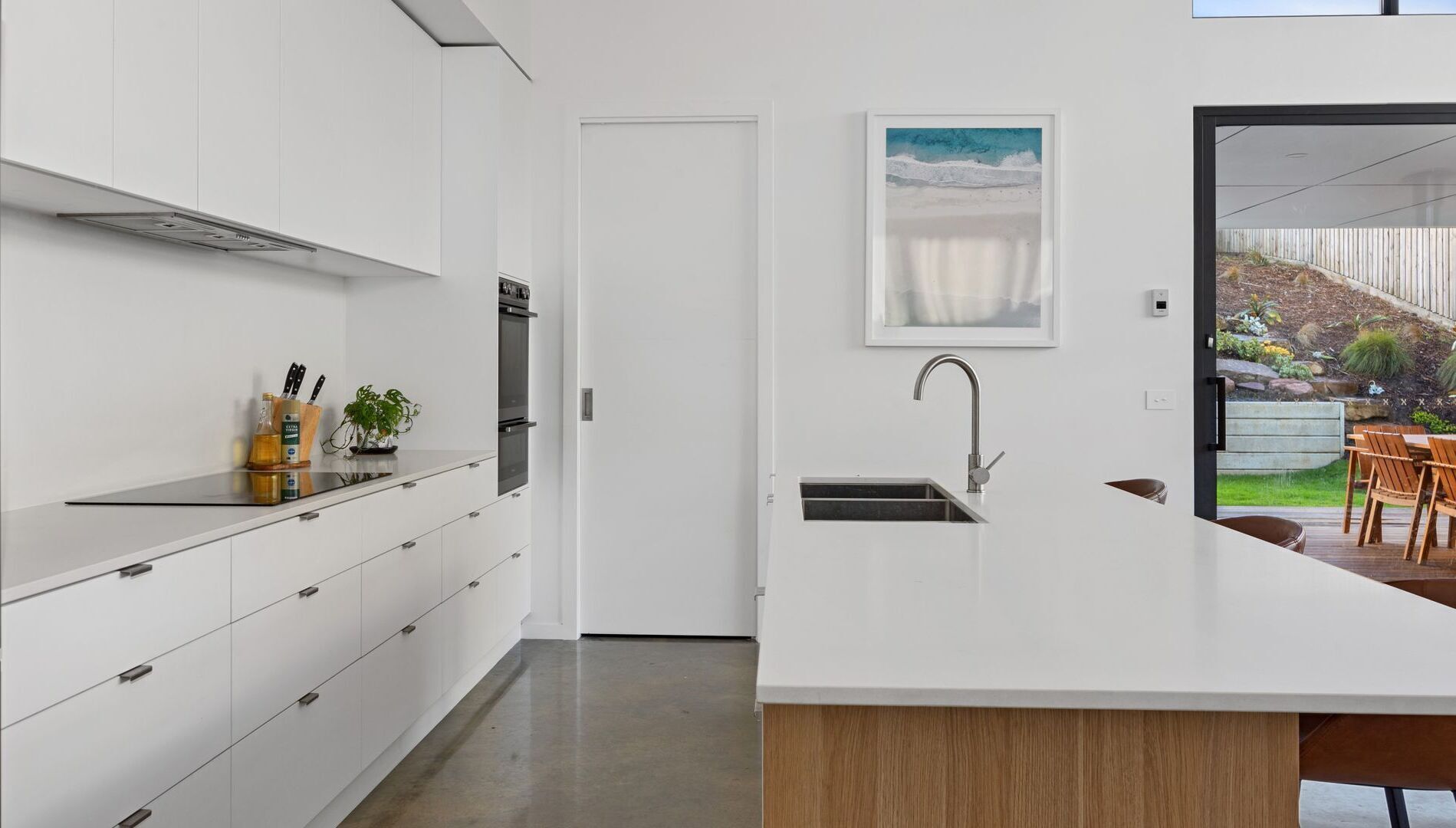 A modern kitchen with white cabinetry, a built-in oven, and a large island with a sink.