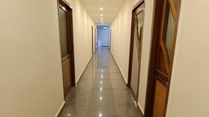 Corredor de hotel com piso brilhante, portas de madeira e tapete de boas-vindas.