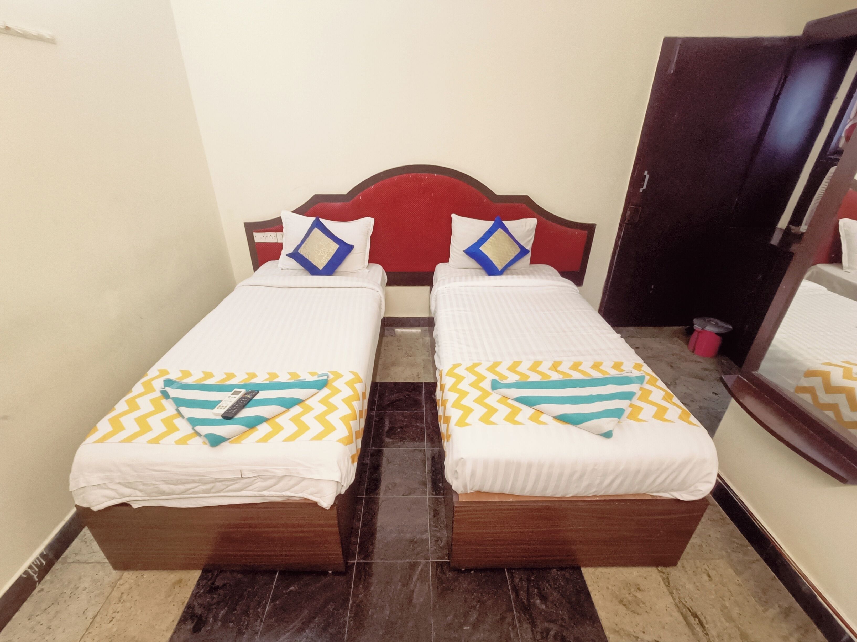 A room with two single beds, each with a patterned bedspread and pillows. The room has a tiled floor and a wooden headboard.